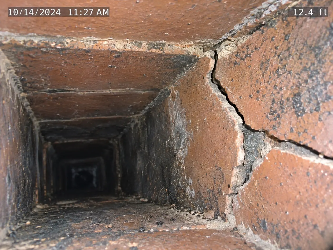 Cracked clay flue tile and open mortar joint seen from inside a chimney during a camera inspection