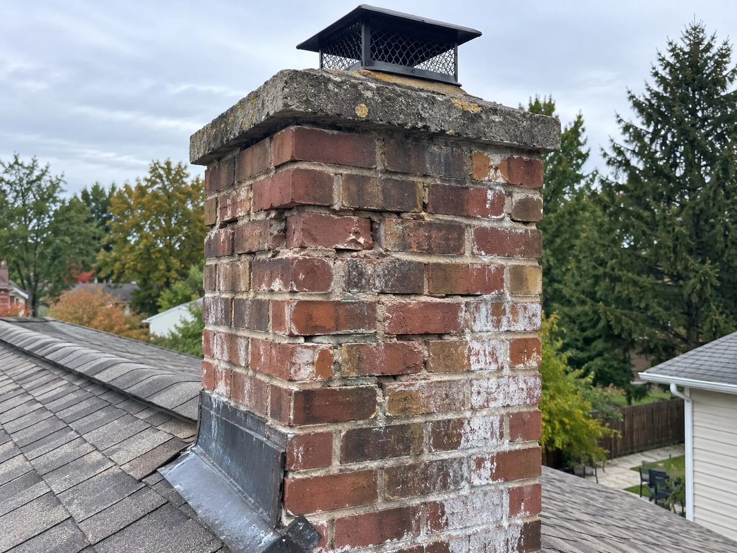 Brick chimney with receded mortar joints, spalled brick faces and white efflorescence staining