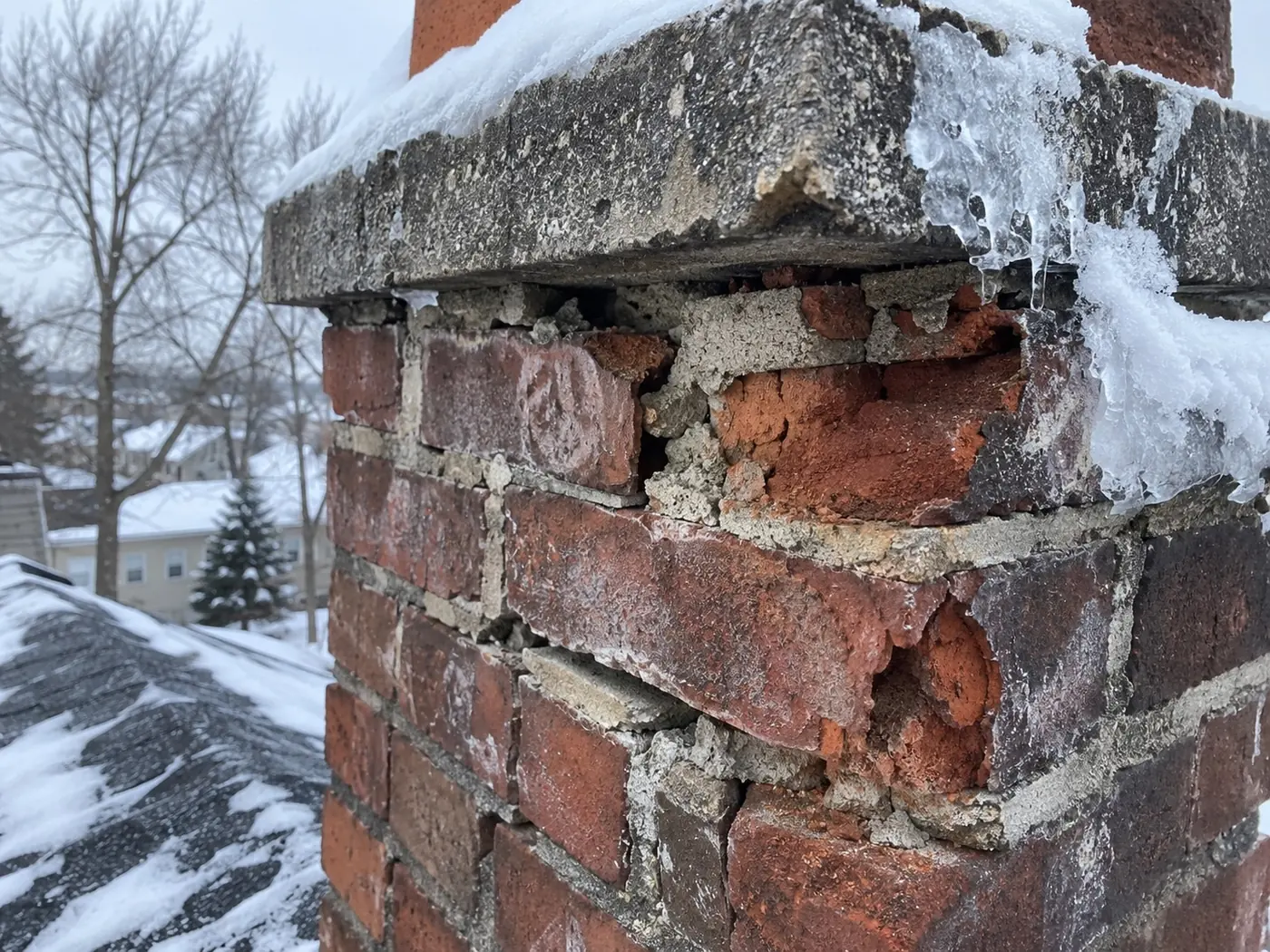 Spalled brick and open mortar joints on a chimney with frost on the surrounding roof