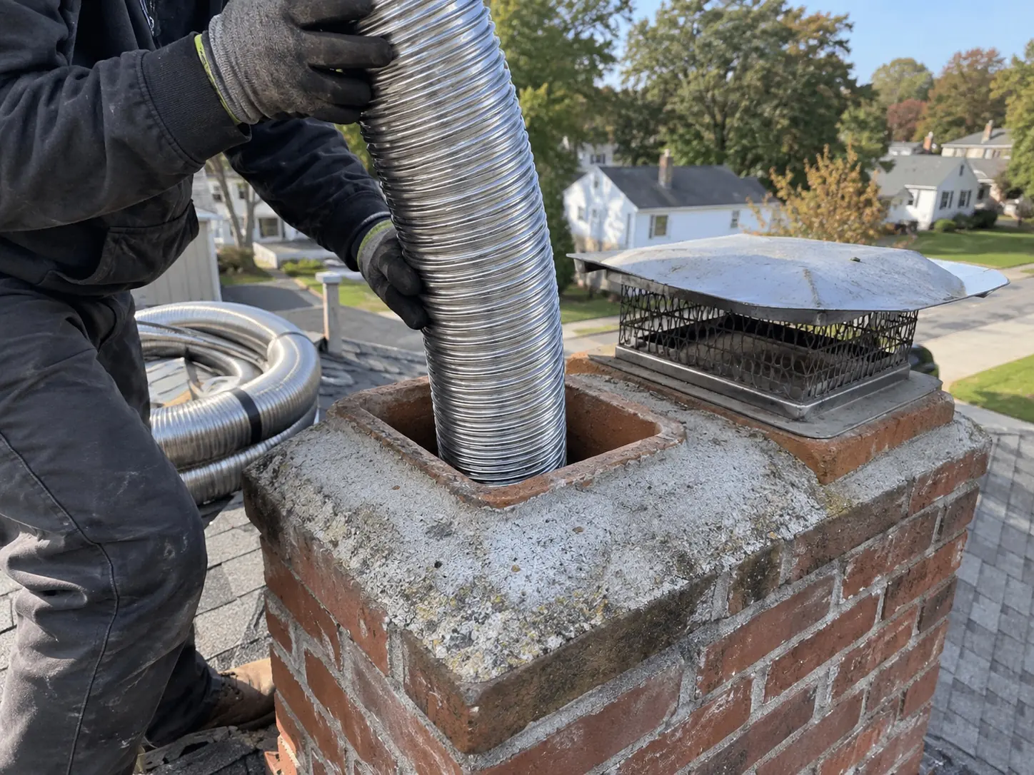 Flexible stainless steel chimney liner being installed down a masonry flue from the roof